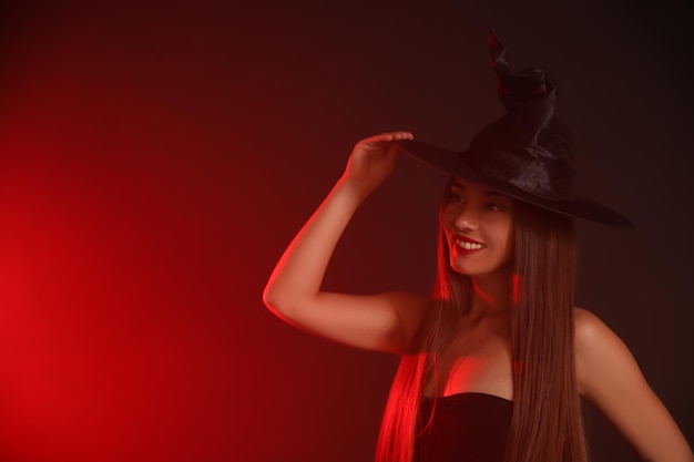 Giovane donna che indossa il costume da strega su sfondo scuro spazio per il testo Festa di Halloween