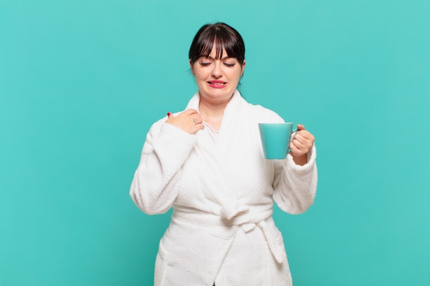 Giovane donna che indossa l'accappatoio si sente stressata, ansiosa, stanca e frustrata, tira il collo della camicia, sembra frustrata dal problema