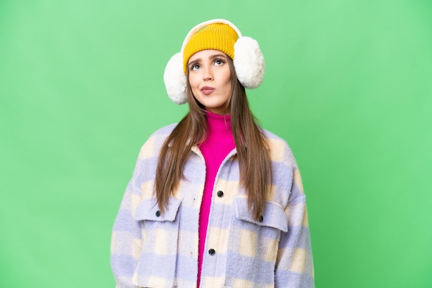 Giovane donna che indossa manicotti invernali su sfondo chroma key isolato e alzando lo sguardo