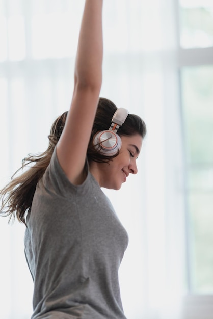 Giovane donna che indossa un auricolare o una cuffia per rilassarsi con una canzone sul letto in camera da letto a casa concetto di suono felice ascolta lo stile di vita in una sensazione audio accogliente