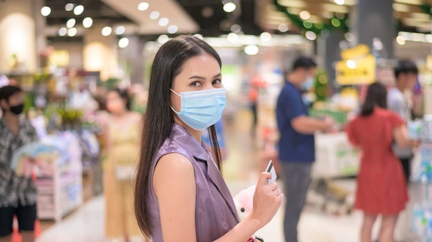 Giovane donna che indossa una maschera chirurgica in attesa in fila vicino alla cassa nel supermercato, covid-19 e concetto pandemico