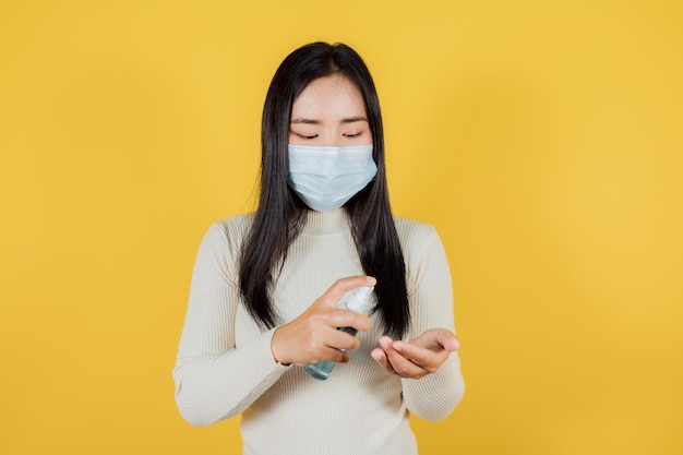 Giovane donna che indossa una maschera medica Premendo il gel alcolico su sfondo giallo, maschera medica per proteggere Covid-19 (Coronavirus)