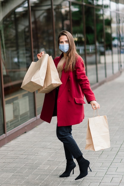 Giovane donna che indossa una maschera per prevenire il virus con borse della spesa su una strada stretta in Europa.