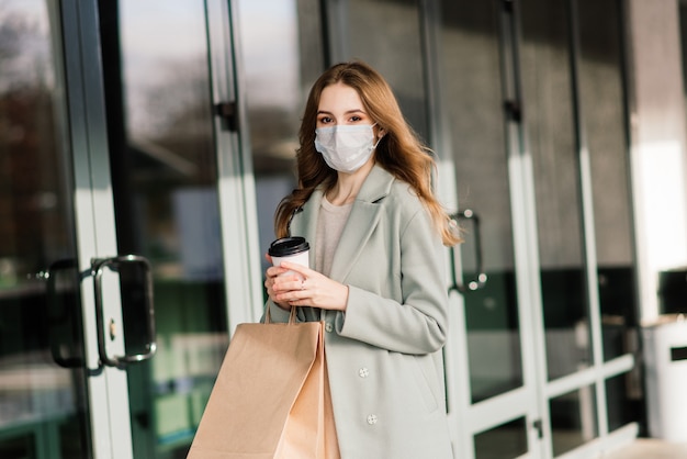 Giovane donna che indossa una maschera per prevenire il virus con borse della spesa su una strada stretta in Europa.