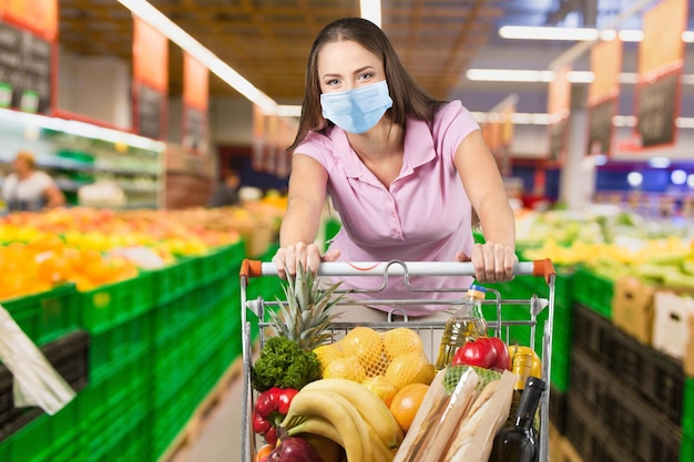 Giovane donna che indossa una maschera protettiva con carrello al supermercato