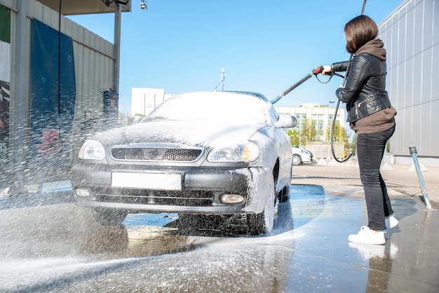 Giovane donna che lava l'auto all'autolavaggio self-service