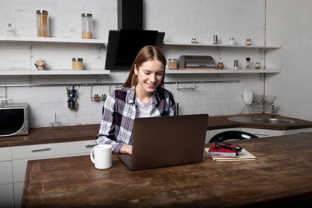 Giovane donna che lavora a casa la mattina. Ragazza che beve caffè. Sta usando il suo laptop