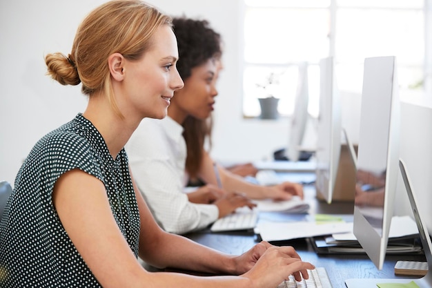 Giovane donna che lavora al computer in ufficio accanto ai colleghi