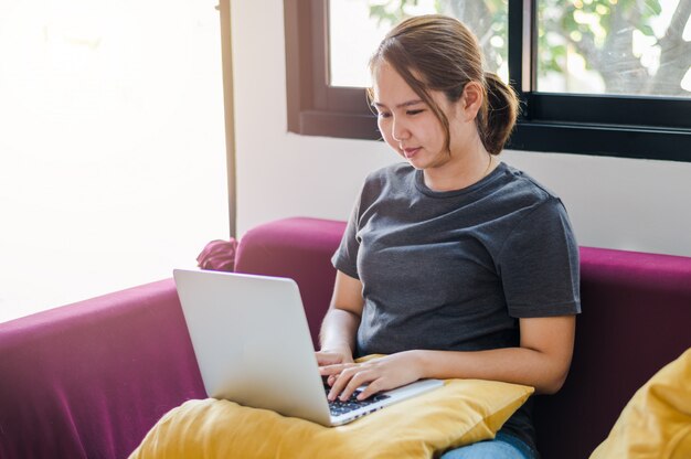 Giovane donna che lavora al computer portatile mentre era seduto sul divano di casa a vivere