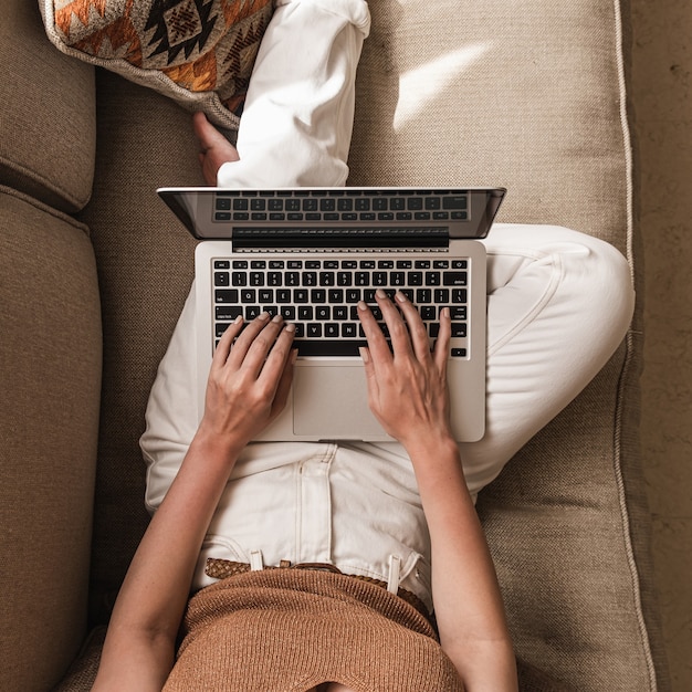 Giovane donna che lavora al computer portatile sdraiata sul divano