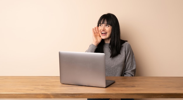 Giovane donna che lavora con il suo computer portatile che grida con la bocca spalancata al laterale