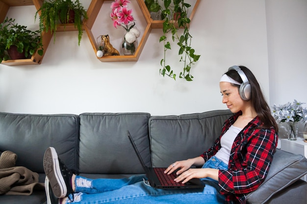 Giovane donna che lavora da casa con il laptop e ascolta la musica con le cuffie