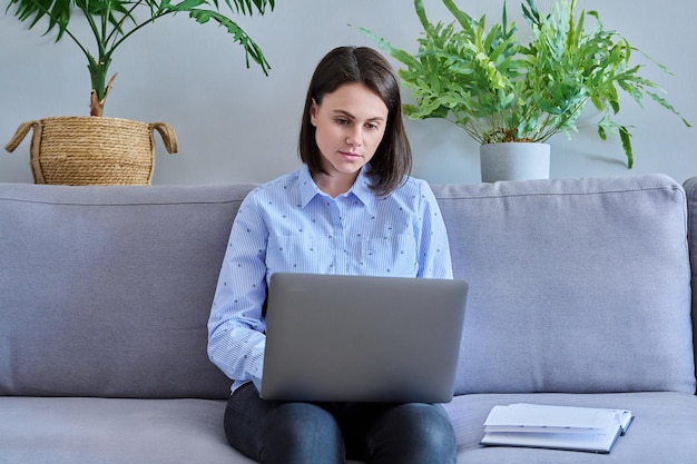 Giovane donna che lavora da casa utilizzando il computer portatile che prende appunti