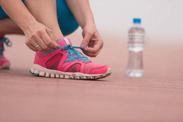 Giovane donna che lega i lacci delle scarpe su scarpe da ginnastica su una passeggiata. In piedi accanto a una bottiglia d'acqua. Esercizio all'aperto