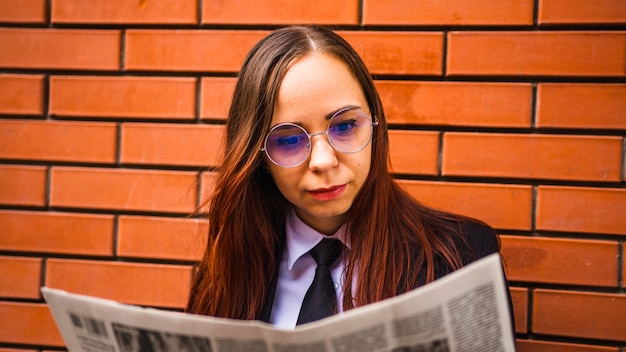 Giovane donna che legge il giornale per strada Signora con i capelli lunghi in abiti casual in piedi sulla strada e leggendo il giornale