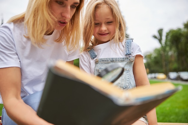 giovane donna che legge un libro interessante per una bambina carina sull'erba verde