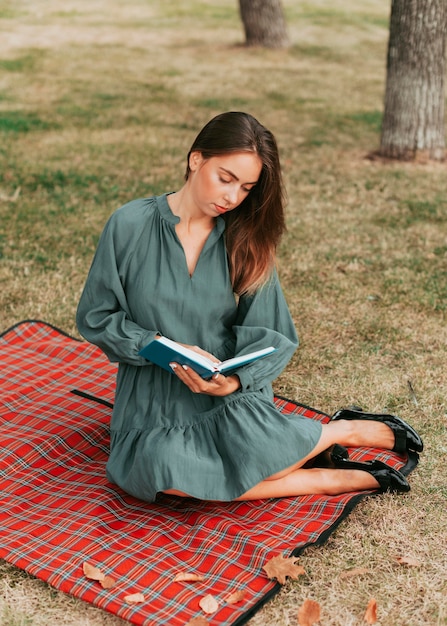 Giovane donna che legge un libro su una coperta da picnic