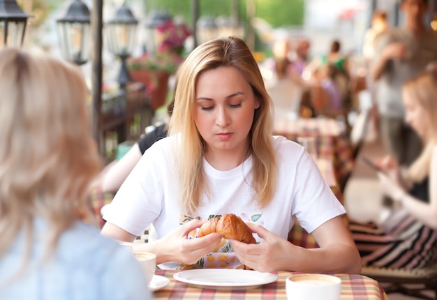 Giovane donna che mangia croissant e beve caffè in una terrazza di un caffè con gli amici