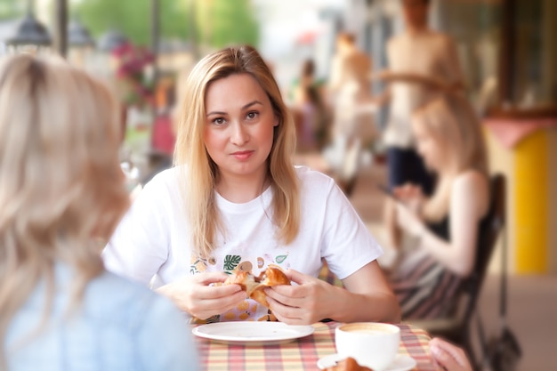 Giovane donna che mangia croissant e beve caffè in una terrazza di un caffè con gli amici