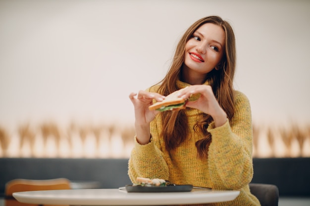 Giovane donna che mangia panino al bar al coperto.