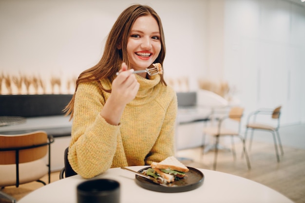 Giovane donna che mangia panino al caffè al coperto