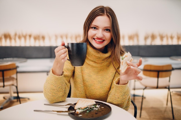 Giovane donna che mangia panino al caffè al coperto