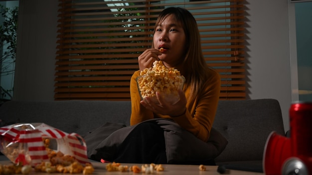 Giovane donna che mangia popcorn e guarda la televisione a casa la sera Attività per il tempo libero relax hobby concetto