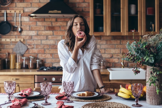 Giovane donna che mangia una ciambella con piacere in cucina.