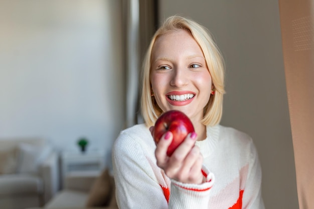 Giovane donna che mangia una mela mordendo davanti alla grande finestra della cucina di casa sua