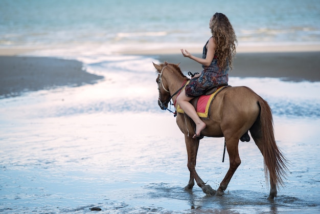 Giovane donna che monta un cavallo sulla spiaggia, concetto di viaggio di vacanze estive.