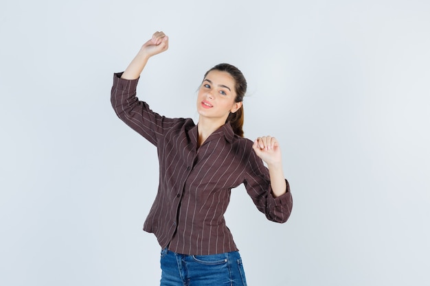 Giovane donna che mostra gesto vincitore in camicia a righe, jeans e guardando fortunato, vista frontale.