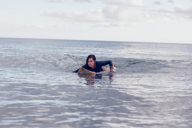 Giovane donna che nuota sopra la tavola da surf in acqua
