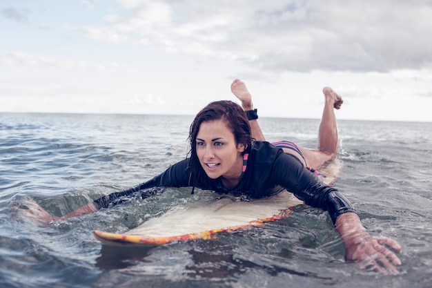 Giovane donna che nuota sopra la tavola da surf in acqua