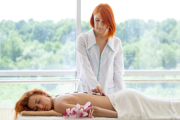 Giovane donna che ottiene massaggio di pietra caldo nel salone della stazione termale