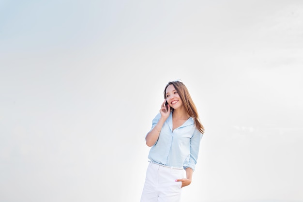 Giovane donna che parla al cellulare Sullo sfondo dello spazio della copia del cielo bianco