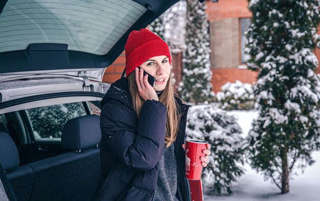 Giovane donna che parla al telefono in piedi vicino all'auto in inverno