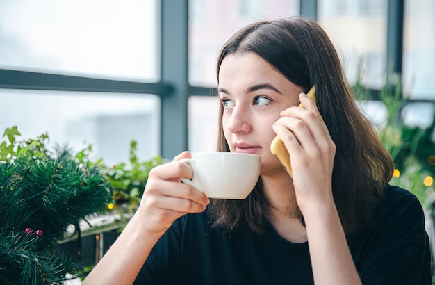 Giovane donna che parla al telefono mentre è seduto vicino alla finestra in un caffè