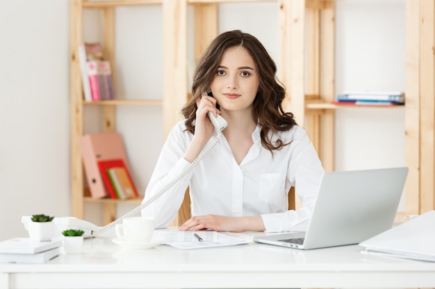 Giovane donna che parla sul telefono in ufficio moderno.