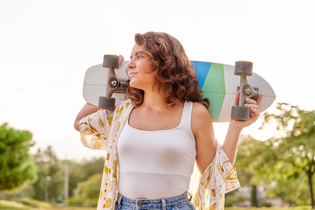 Giovane donna che pattina su un incrociatore con un longboard sulle spalle