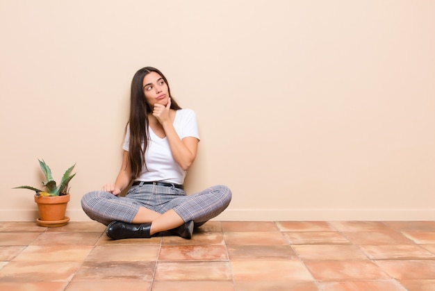 Giovane donna che pensa, si sente dubbiosa e confusa, con diverse opzioni, chiedendosi quale decisione prendere seduto su un piano