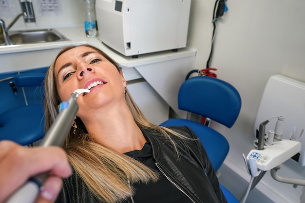 Giovane donna che posa con la bocca mezzo aperta alla sedia del dentista strumento dentale vicino ai suoi denti vista in prima persona