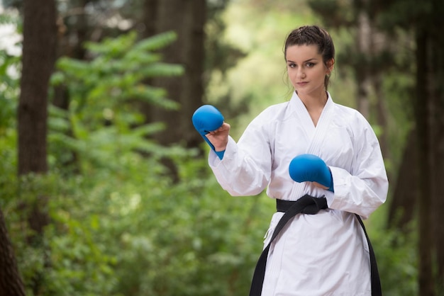 Giovane donna che pratica il suo karate si muove nella zona boscosa della foresta Kimono bianco Cintura nera