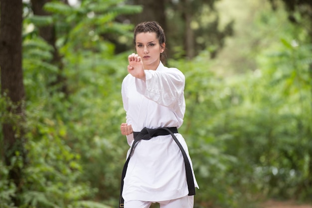 Giovane donna che pratica il suo karate si muove nella zona boscosa della foresta Kimono bianco Cintura nera