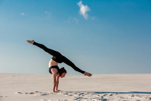 Giovane donna che pratica la verticale sulla spiaggia con sabbia bianca e cielo blu brillante