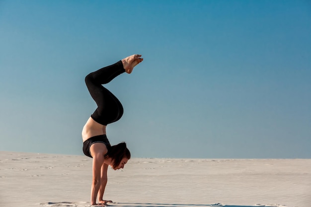 Giovane donna che pratica la verticale sulla spiaggia con sabbia bianca e cielo blu brillante