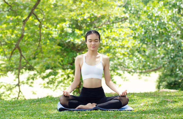 Giovane donna che pratica lo yoga nella natura, donna asiatica sta praticando lo yoga nel parco cittadino