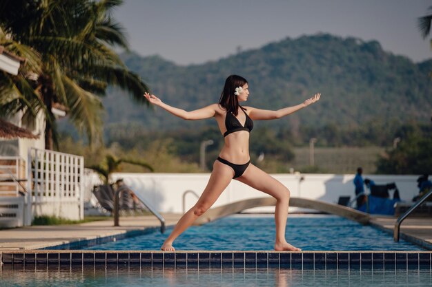 Giovane donna che pratica posa yoga sulla piscina e la spiaggia naturale al tramonto o all'alba Yoga e concetto sano Warrior I o Virabhadrasana Pose