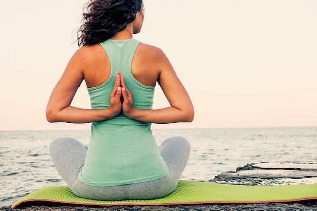 Giovane donna che pratica yoga in riva al mare