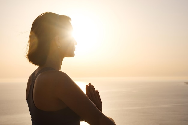 Giovane donna che pratica yoga sul mare al tramonto