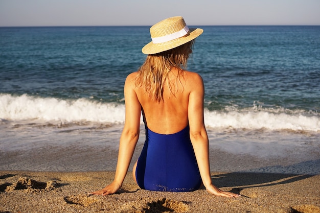 Giovane donna che prende il sole in spiaggia tropicale donna in costume da bagno blu e cappello